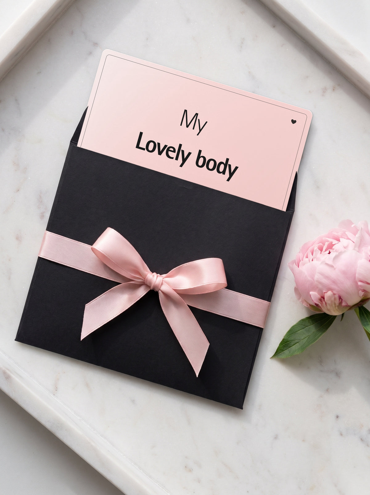 Carte cadeau My Lovely Body glissée dans une pochette noire nouée d'un ruban rose poudré, avec une pivoine